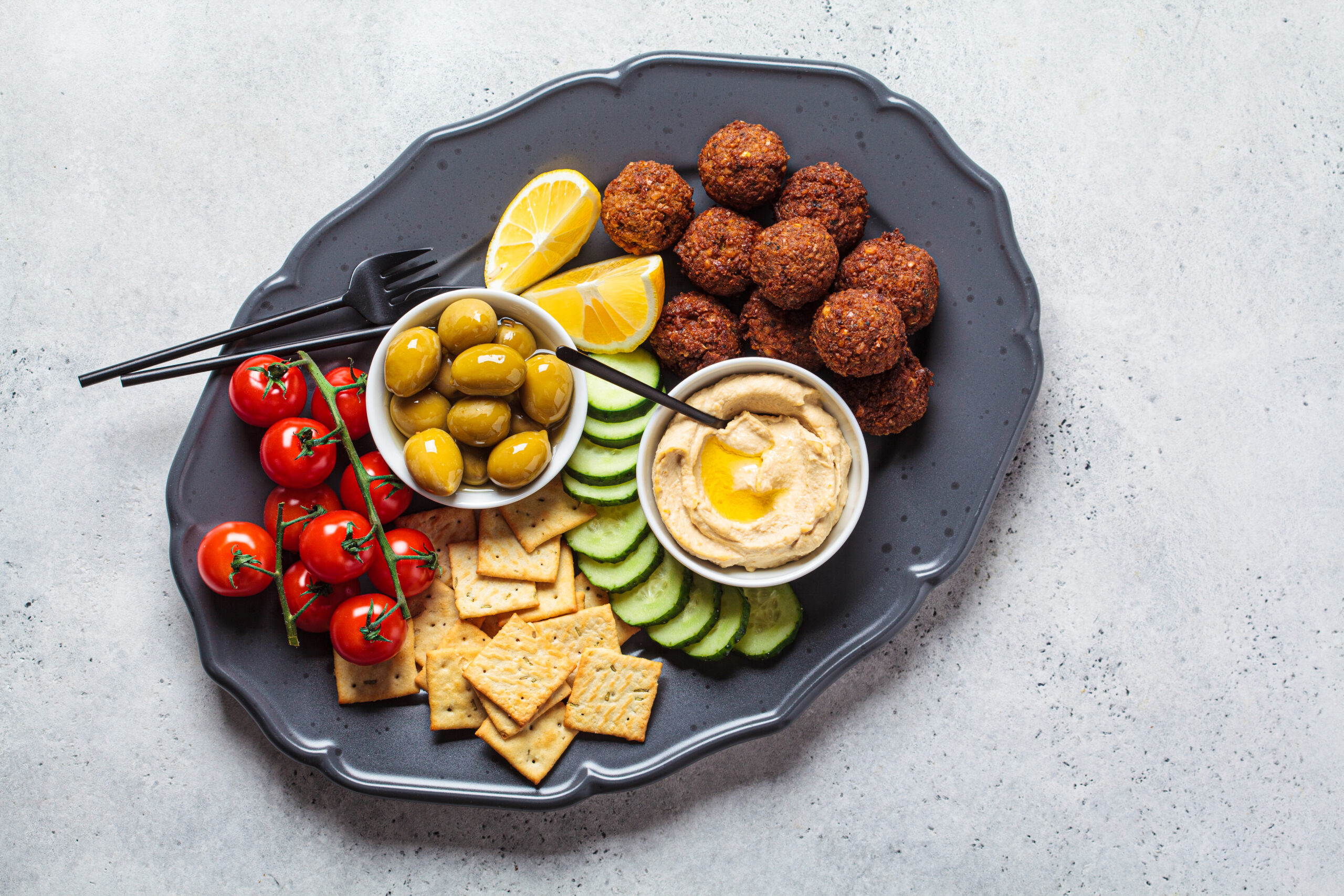 Falafel platter with hummus, olives, crackers and vegetables, top view. Healthy vegan food concept.